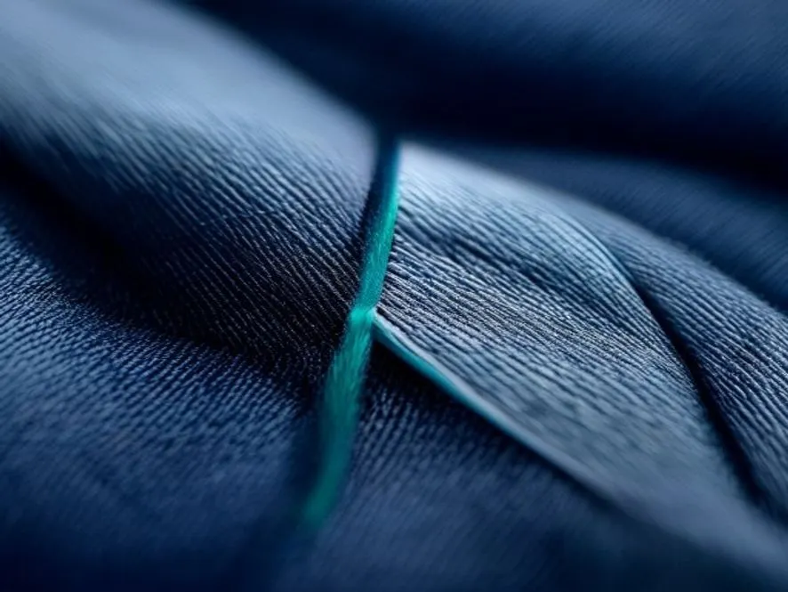 Macro detail of a navy woven textile crossed by a single teal thread